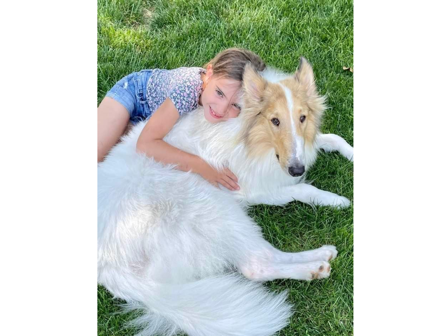 A girl and her dog laying on the grass.